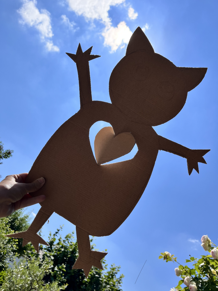 Ausgeschnittene Katzenfigur aus Pappe mit Herz vor blauem Himmel